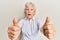 Senior grey-haired woman doing thumbs up positive gesture afraid and shocked with surprise and amazed expression, fear and excited