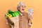 Senior grey-haired woman holding groceries and canadian dollars angry and mad screaming frustrated and furious, shouting with