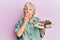 Senior grey-haired woman holding plate with cake slices covering mouth with hand, shocked and afraid for mistake