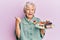 Senior grey-haired woman holding plate with cake slices pointing thumb up to the side smiling happy with open mouth