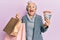 Senior grey-haired woman holding shopping bags and australia dollars smiling and laughing hard out loud because funny crazy joke