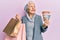 Senior grey-haired woman holding shopping bags and australia dollars smiling looking to the side and staring away thinking