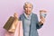 Senior grey-haired woman holding shopping bags and australia dollars sticking tongue out happy with funny expression