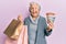 Senior grey-haired woman holding shopping bags and australia dollars winking looking at the camera with sexy expression, cheerful