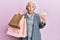 Senior grey-haired woman holding shopping bags and euros banknotes making fish face with mouth and squinting eyes, crazy and