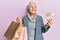 Senior grey-haired woman holding shopping bags and south korea won banknotes smiling looking to the side and staring away thinking