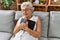 Senior grey-haired woman hugging bible sitting on sofa at home