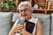 Senior grey-haired woman hugging bible sitting on sofa at home