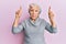 Senior grey-haired woman pointing up with fingers clueless and confused expression