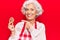 Senior grey-haired woman wearing apron holding cookie smiling happy pointing with hand and finger