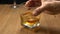 Senior hand hold the glass of whiskey on a wooden table, shake it and lift it for drinking.