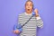 Senior handsome grey-haired man holding vintage handset telephone over purple background scared in shock with a surprise face,