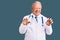 Senior handsome grey-haired man wearing doctor coat and stethoscope smiling funny doing claw gesture as cat, aggressive and sexy