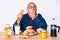 Senior handsome man with gray hair sitting on the table eating breakfast in the morning covering mouth with hand, shocked and