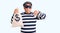 Senior handsome man wearing burglar mask holding money bag with angry face, negative sign showing dislike with thumbs down,