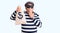 Senior handsome man wearing burglar mask holding money bag covering mouth with hand, shocked and afraid for mistake