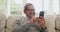 Senior, happy man and typing with phone in home for social media, reading news article and information with glasses