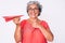 Senior hispanic grey- haired woman holding paper airplane smiling happy pointing with hand and finger