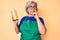 Senior hispanic grey- haired woman wearing apron holding scourer serious face thinking about question with hand on chin,