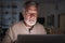 Senior Hispanic man checking his finances online at home using a laptop computer at night, close up