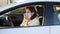 Senior Hispanic woman with face mask driving her car with her arm leaning on the window.