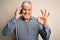 Senior hoary man having conversation talking on the smartphone over white background doing ok sign with fingers, excellent symbol