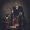 Senior hunter with a english setter and shotgun in a traditional shooting clothing, sitting on a dark background.