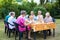 Senior ladies attending art classes outdoors seated around a table working on their paintings using model pictures on easels