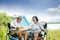 Senior lovers camping on the waterfront, sit on a chair, view tourist map