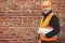 Senior male foreman in hardhat standing with blueprints at masonry brick wall at building new house. Portrait of happy man