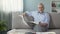 Senior male sitting on couch and reading newspaper, morning ritual, press
