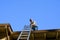 Senior man on apartment building roof ready to climb down an aluminum extension ladder