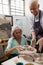 Senior man assisting senior woman in making pottery during drawing class