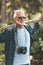 Senior man with beard walks through woods, healthy active lifestyle. Vertical portrait of senior citizen with camera in park
