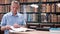 Senior man with books in library. Senior student working in library.