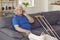 Senior man with broken leg sitting on couch at home and making call on smartphone