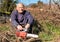 Senior man with chainsaw sitting to rest