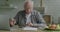 Senior man checking bills counting money concentrated on payment sitting at table at home