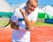 Senior man with elbow pain standing during tennis match on sunny day