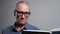 Senior man in elegant glasses reads book on grey background