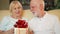 Senior man giving birthday anniversary present golden gift box to wife. Valentine`s Day celebration