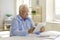 Senior man with glasses sitting at a table at home using a tablet reads information on the Internet.