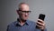 Senior man in glasses tries to read message in smartphone