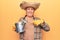 Senior man with grey hair wearing gardener hat holding watering can smiling happy pointing with hand and finger