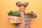 Senior man with grey hair wearing gardener hat holding wooden plant pot smiling happy pointing with hand and finger