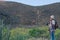 Senior man hiking in arid landscape with mountain, cactus, holding backpack and binoculars