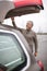 Senior man by his car, closing the trunk lid in a mall parking