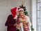 Senior man kissing the cheek of his wife with Christmas gift in hand at home in the living room. romantic couple with Santa hat