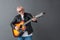 Senior man in leather jacket and sunglasses standing isolated on gray playing guitar singing joyful