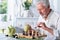 Senior man looking at chess board while drinking tea at home